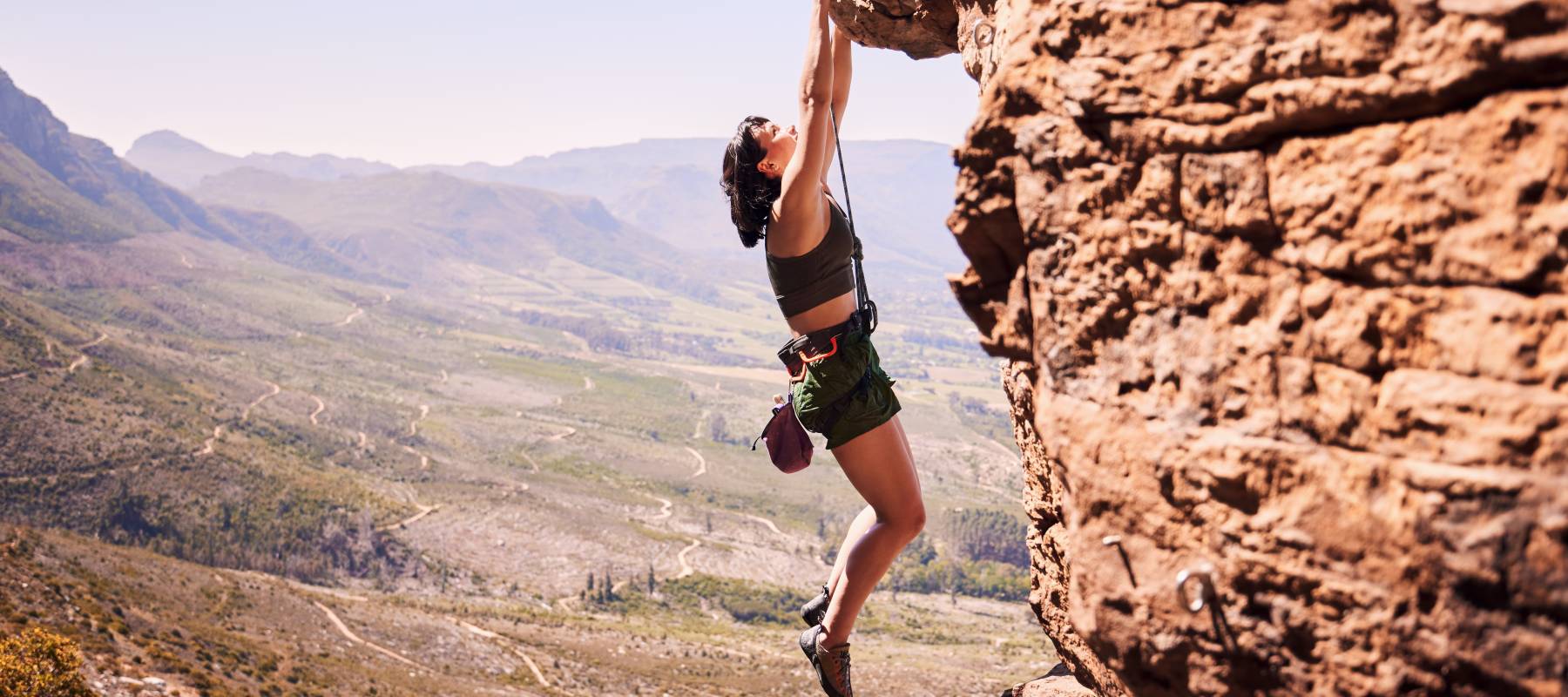 A rock climbing woman hanging on to a cliff.