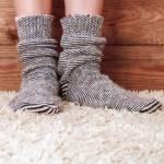 Legs of a woman in gray socks on the carpet on the wooden background. Vintage toning