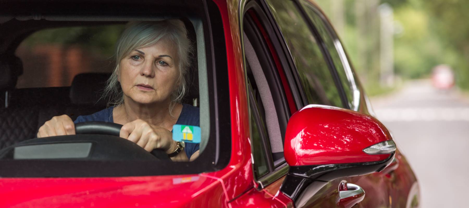 older lady with concerned expression at the wheel of a red car
