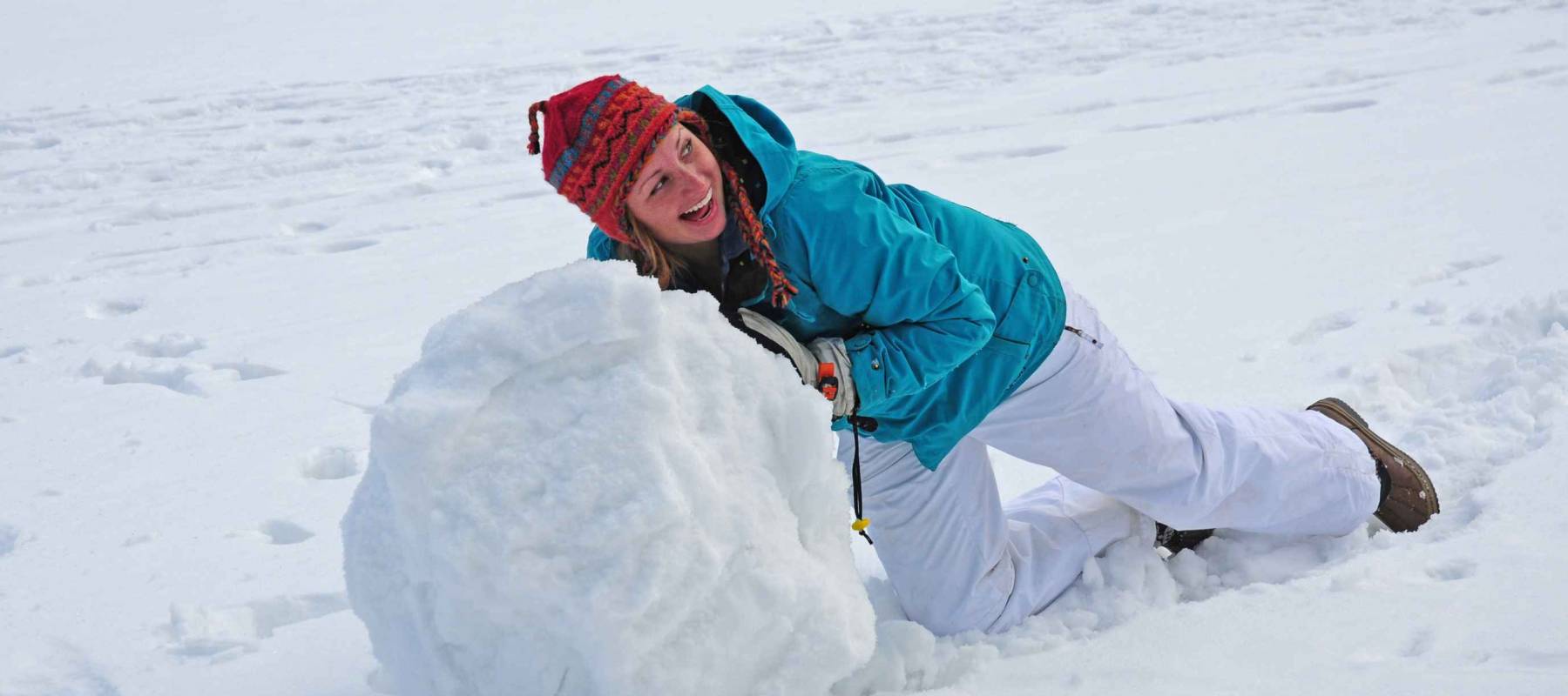 Young college-age woman rolling giant snowball to make snowman