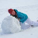 Young college-age woman rolling giant snowball to make snowman