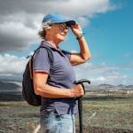 senior Caucasian woman walking on hiking day on outdoor trail on excursion between sea and countryside