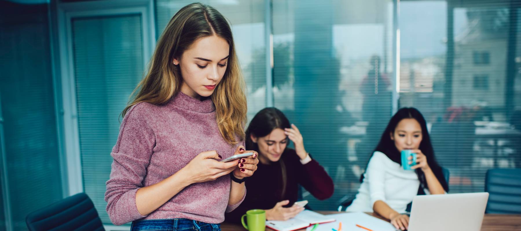 young worker wearing jeans sits on office table looking at phone