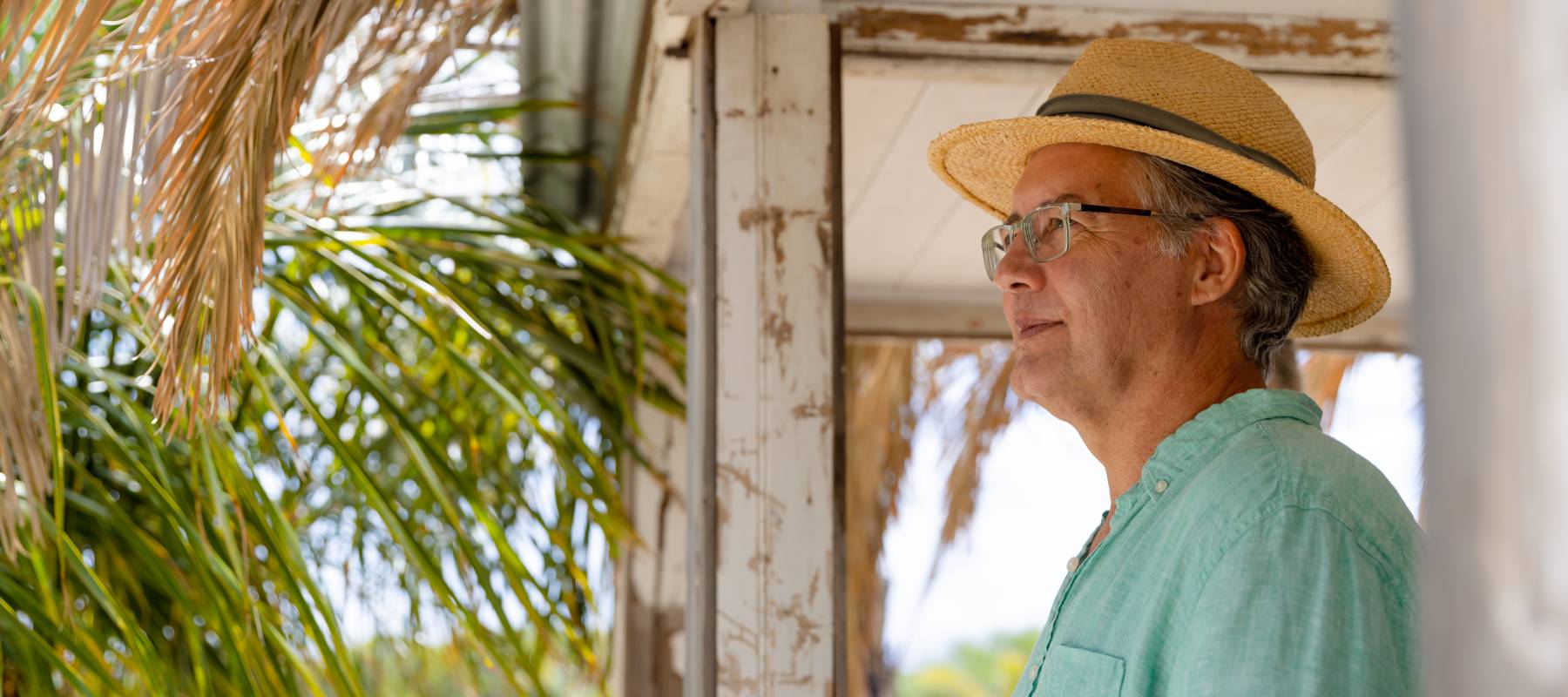 Side view of thoughtful senior man wearing hat standing in balcony at cottage.