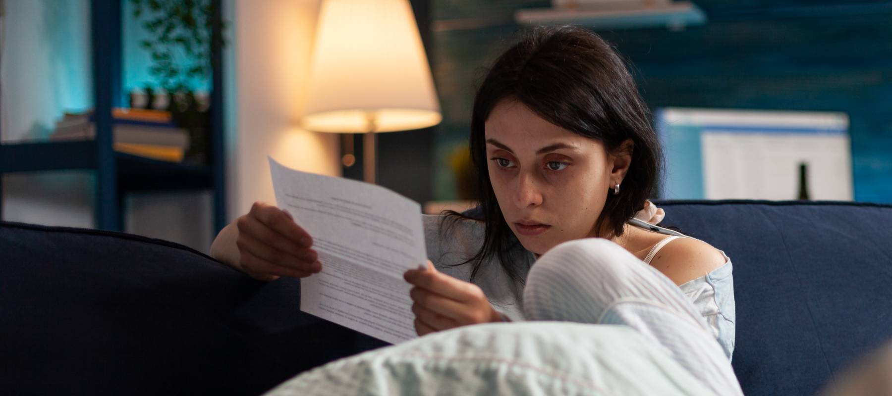 Woman on the couch looking very scared and staring at a piece of paper