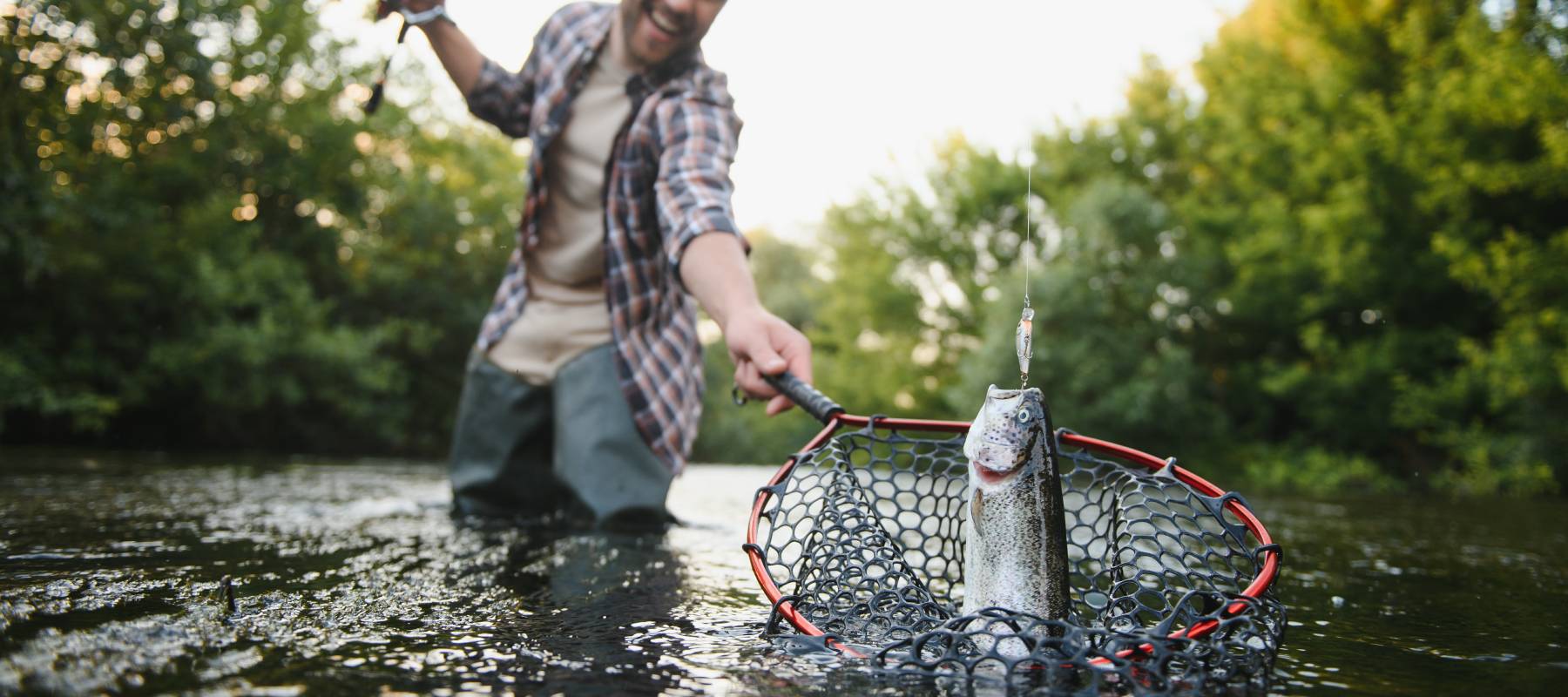 Man with fishing rod, catching a catfish in a net, close up, standing in a river outdoors.