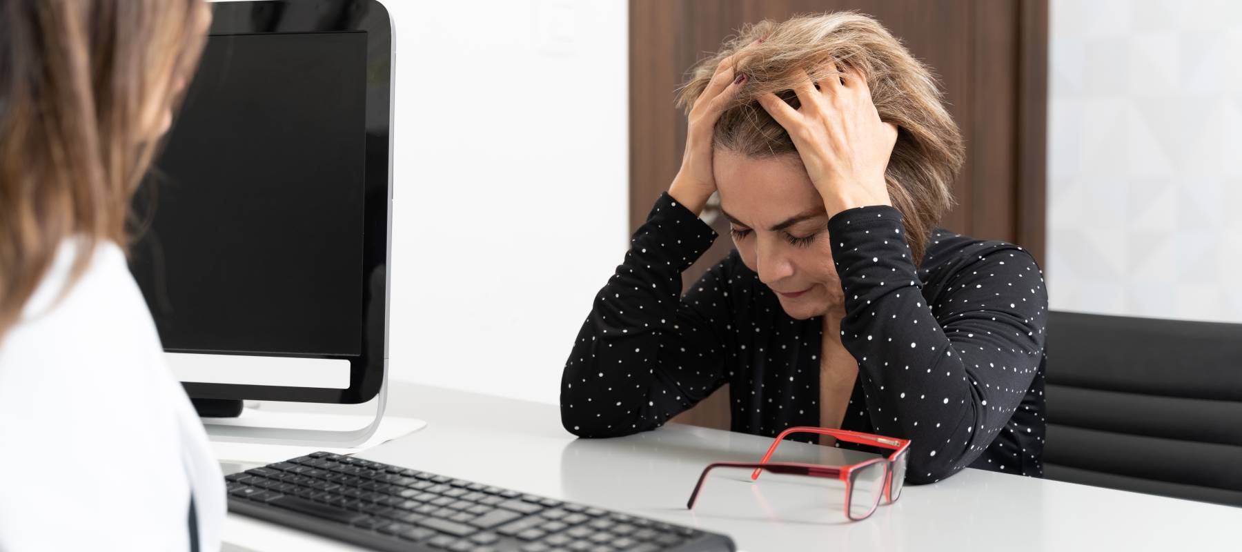 A businesswoman upset, sitting at the desk of another businesswoman.