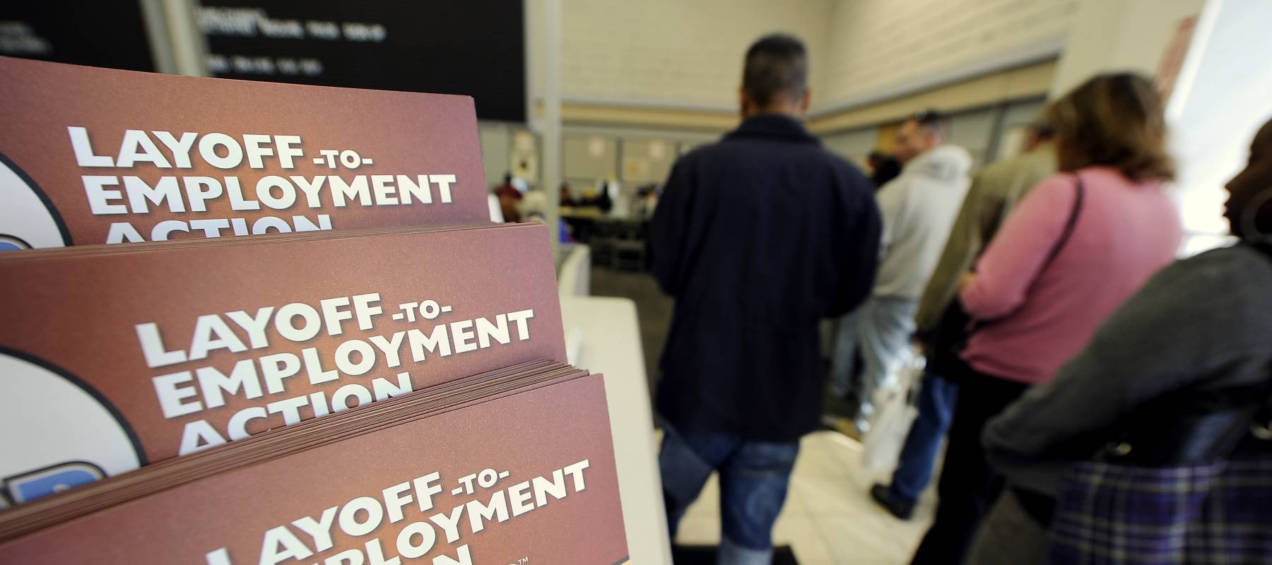 Job-seekers wait in line for assistance at a government-run employment center. Close up of "lay-off" leaflets.