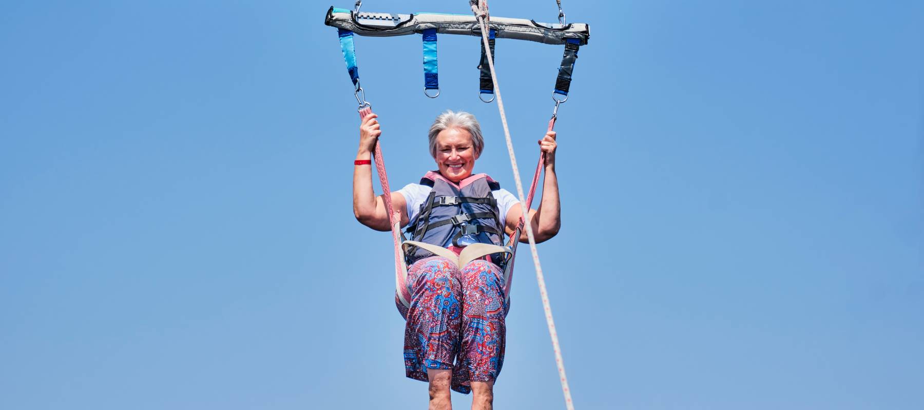 Woman with gray hair with a big smile and a fearless expression parasailing.