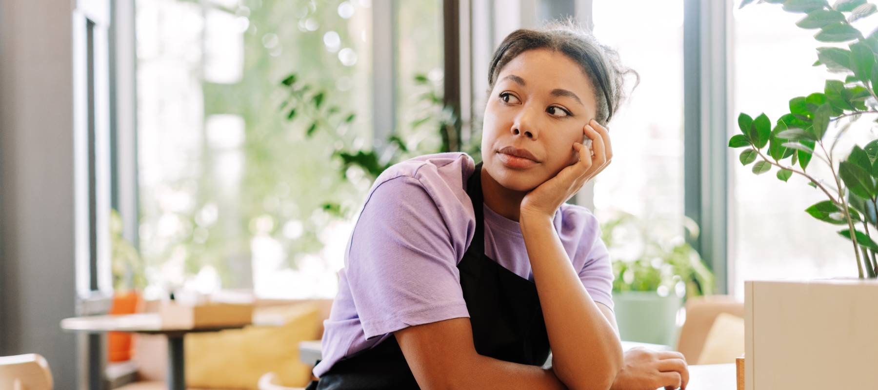 tired waitress leaning on a table in a coffee shop looking away pensively