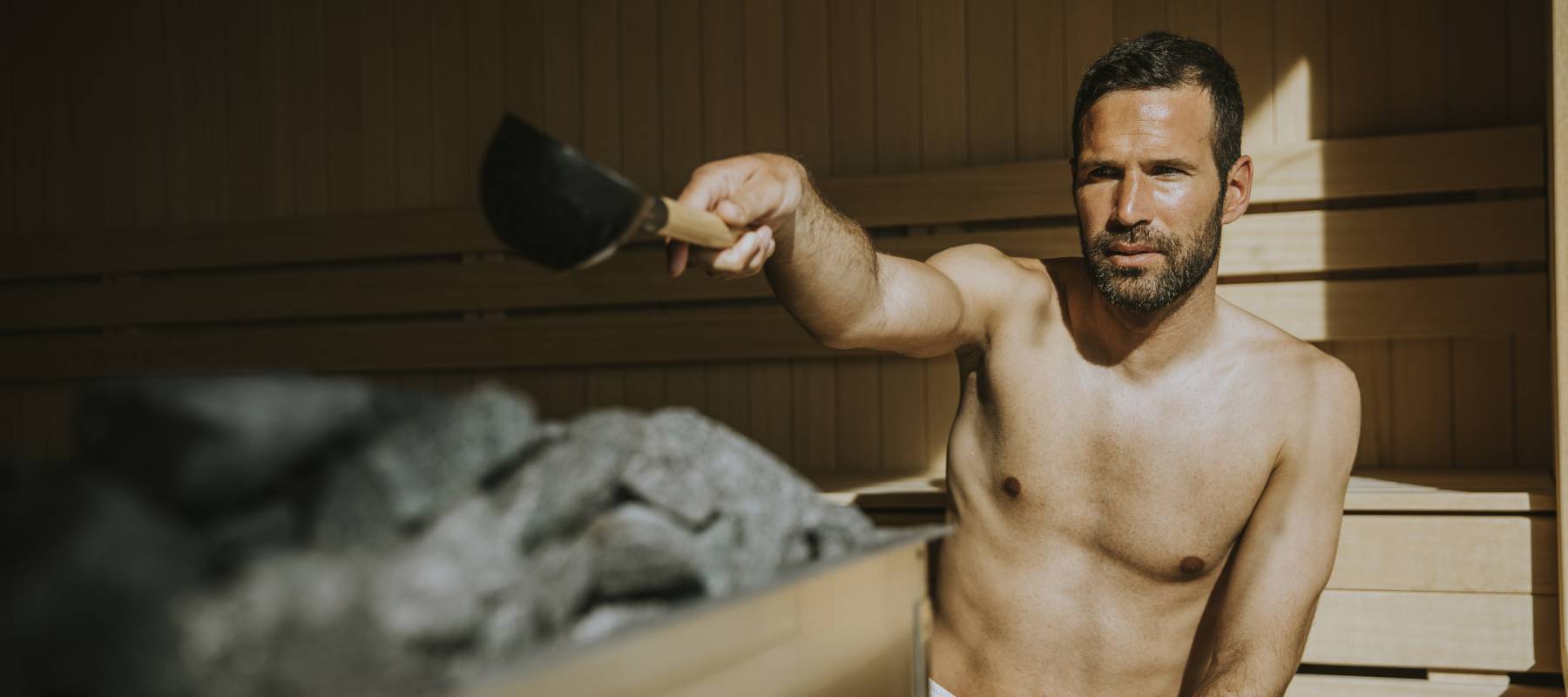 Man pouring water onto hot stone in the sauna.