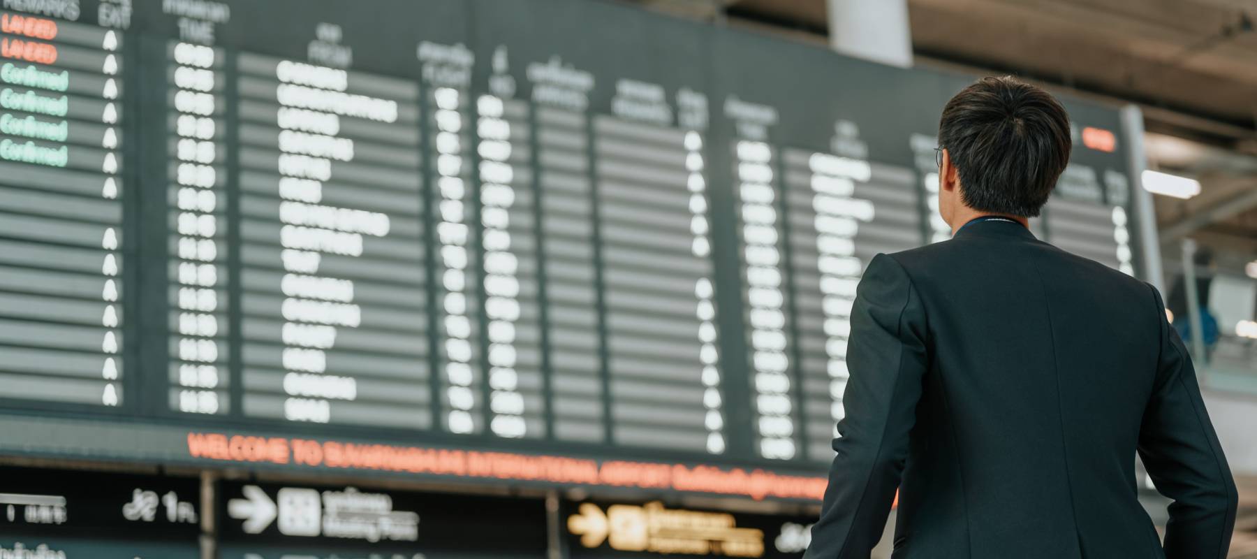 Young businessman staring up at timetable screen board in airport.