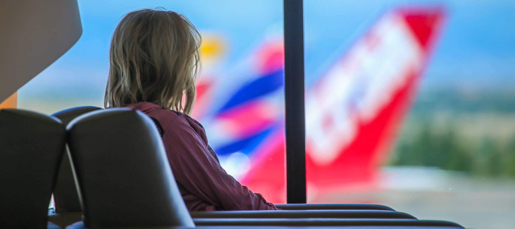 woman see from the the back in an airport lounge looking out over tarmac at planes