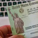 Hand holding stimulus check bearing President Donald Trump's name