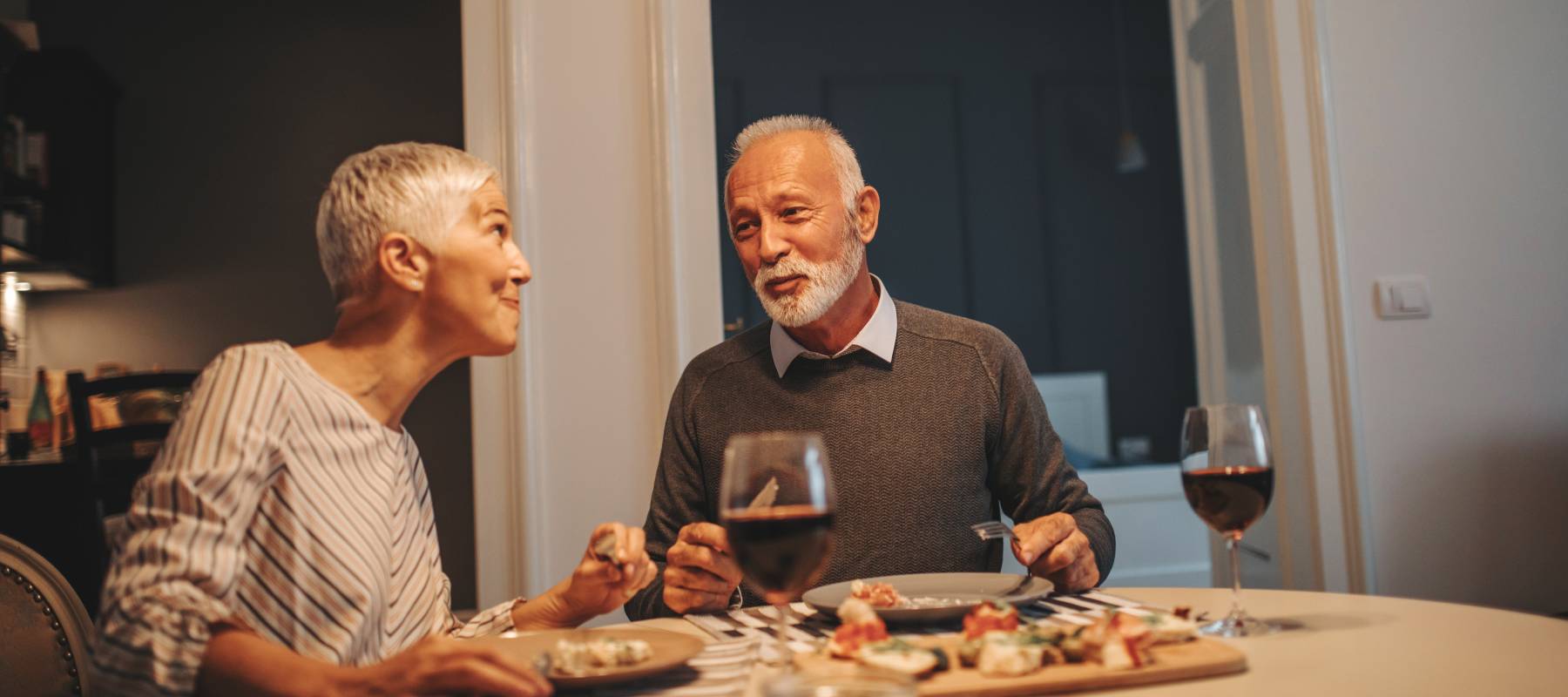 senior Caucasian couple enjoying meal and wine together at home
