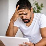 African-American man wearing white V-neck T-shirt looks at disturbing financial documents
