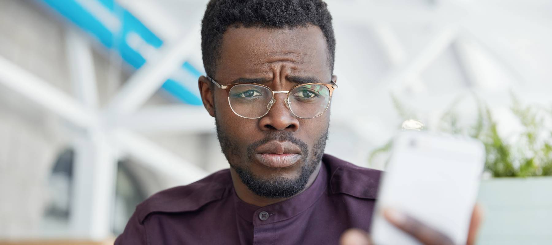 unhappy Black male office manager looks with upset expression at smart phone