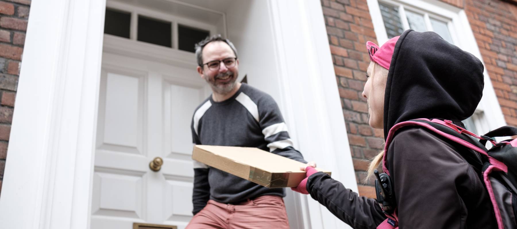 Side view of smiling bike courier woman holding a parcel from a middle-aged bespectacled man.