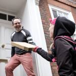 Side view of smiling bike courier woman holding a parcel from a middle-aged bespectacled man.