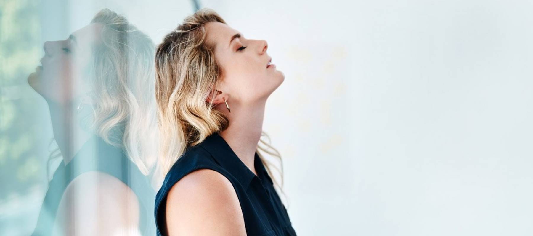 Stressed-out woman with long blonde hair leans back against a window