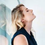 Stressed-out woman with long blonde hair leans back against a window