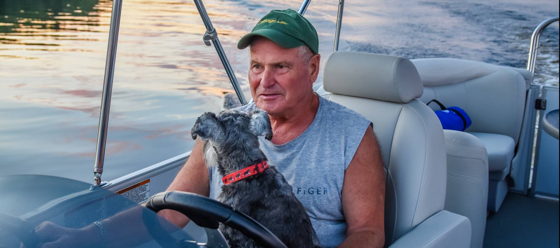 Man driving pontoon boat with dog in his lap.