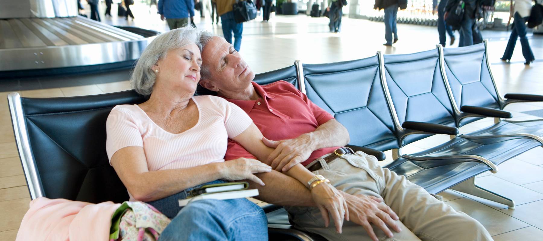 medium shot of a senior Caucasian couple sleeping together while waiting on chairs in an airport terminal