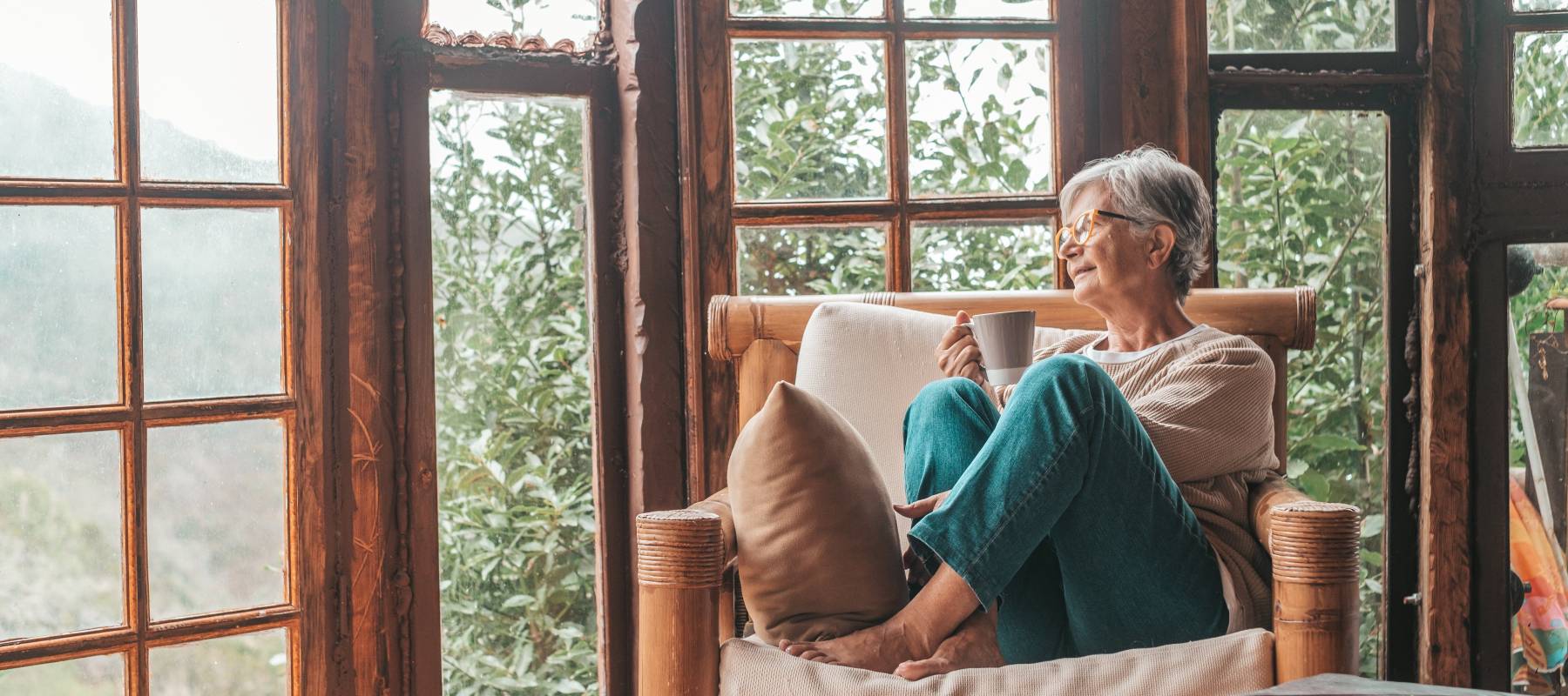 senior Caucasian woman sitting on sofa and holding coffee mug while looking away at home