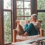 senior Caucasian woman sitting on sofa and holding coffee mug while looking away at home