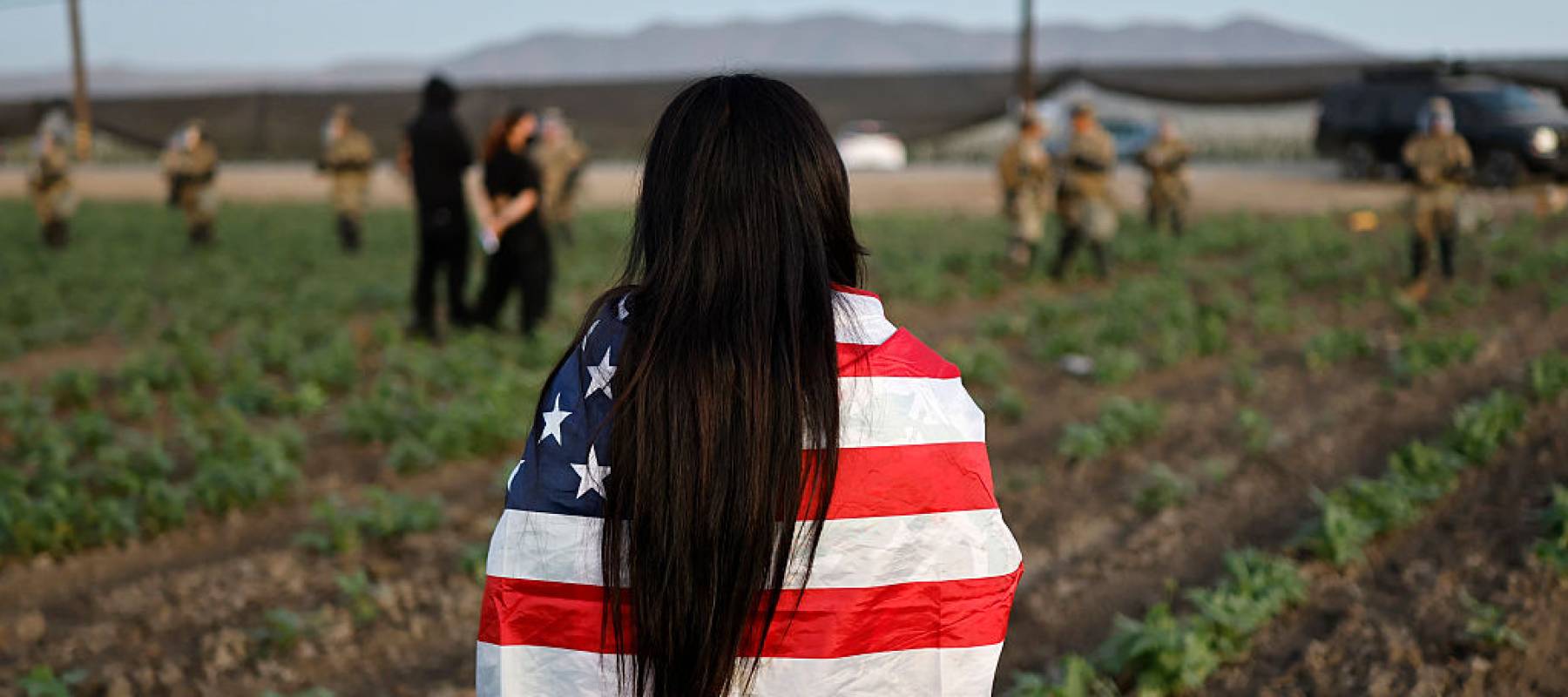 A demonstrator wrapped in an American flag watches an ICE raid at a California farm.