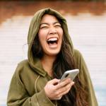Young Asian-American woman in green hoodie is ecstatic over something on her smartphone