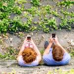 A couple stand side by side on their smartphones.