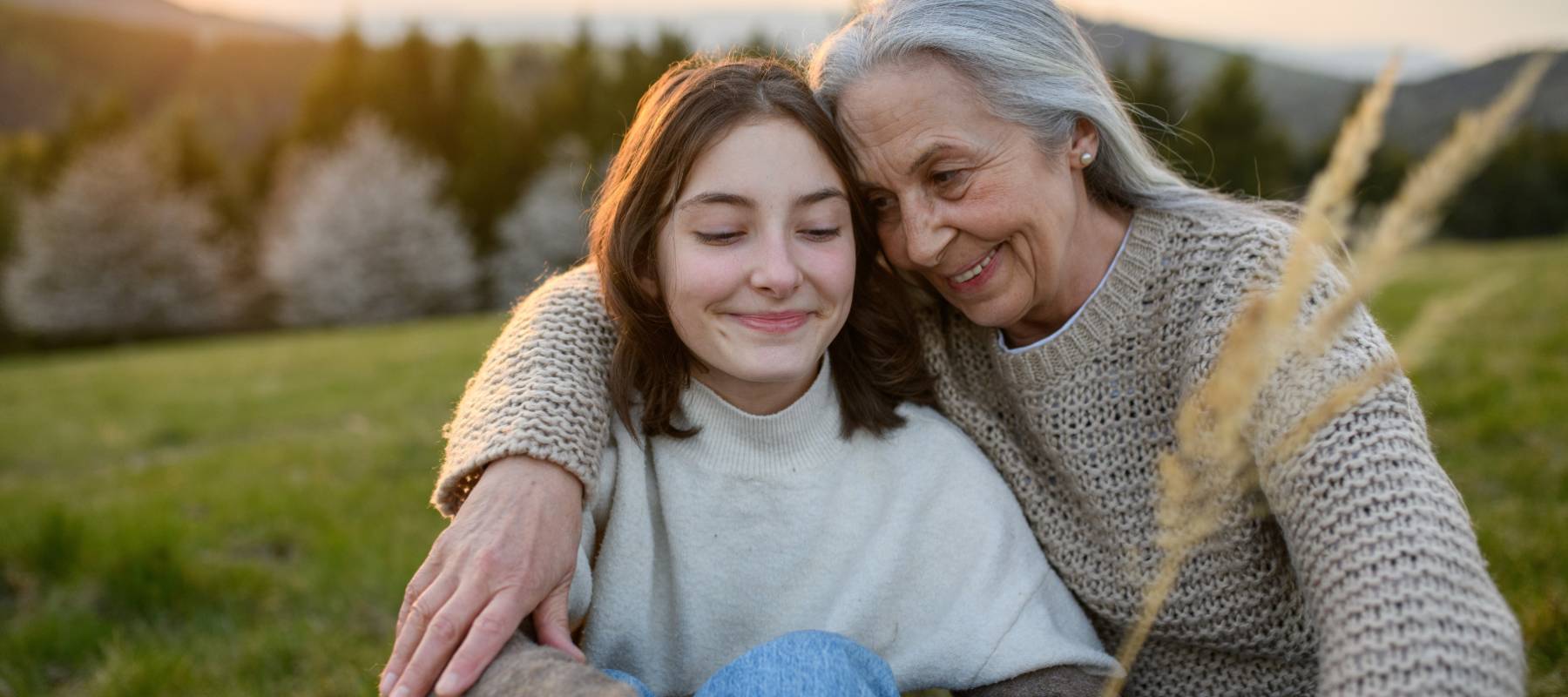 older Caucasian woman hugging a younger woman and smiling outside on a hill