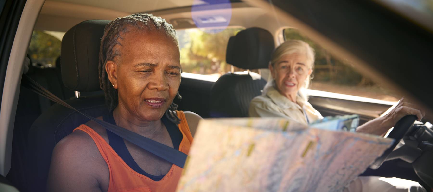 Two seniors in a car trying to find their location on a map.
