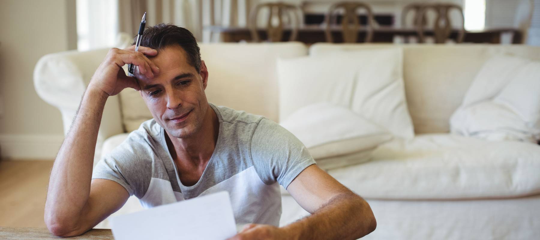 Caucasian man sitting on floor in living room using pen reviewing chart papers at low coffee table
