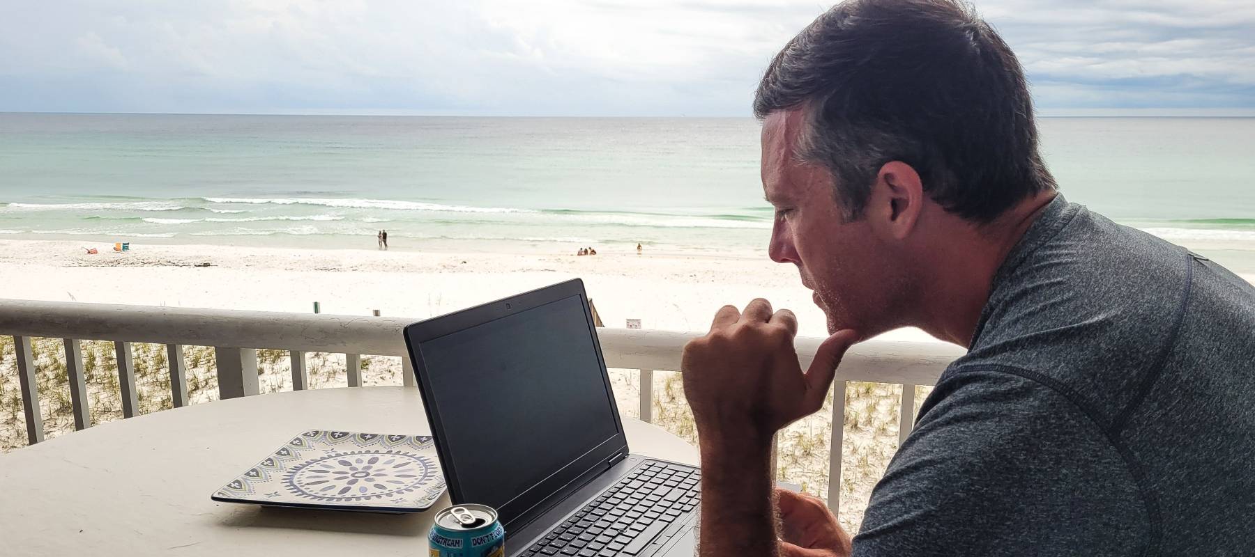 A man works remotely from a tropical location with a beach view.