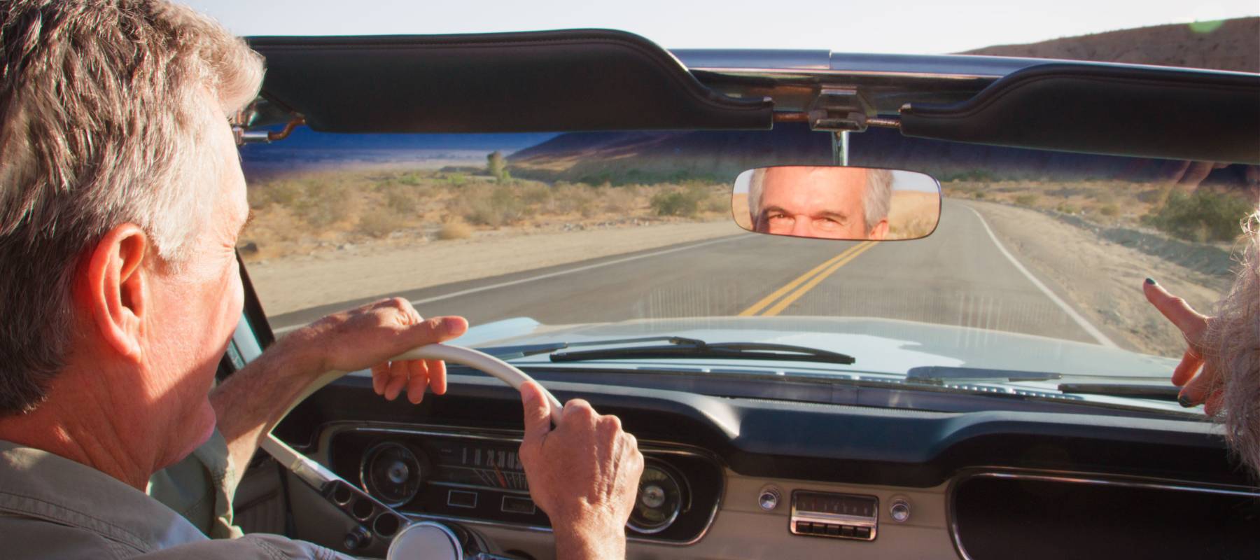 A couple driving a classic convertible along a country road.
