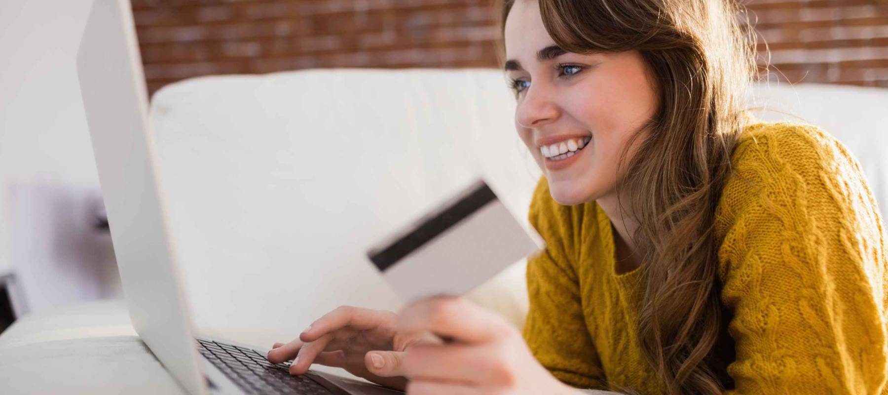 Young woman using her credit card to buy online sitting on the couch at home