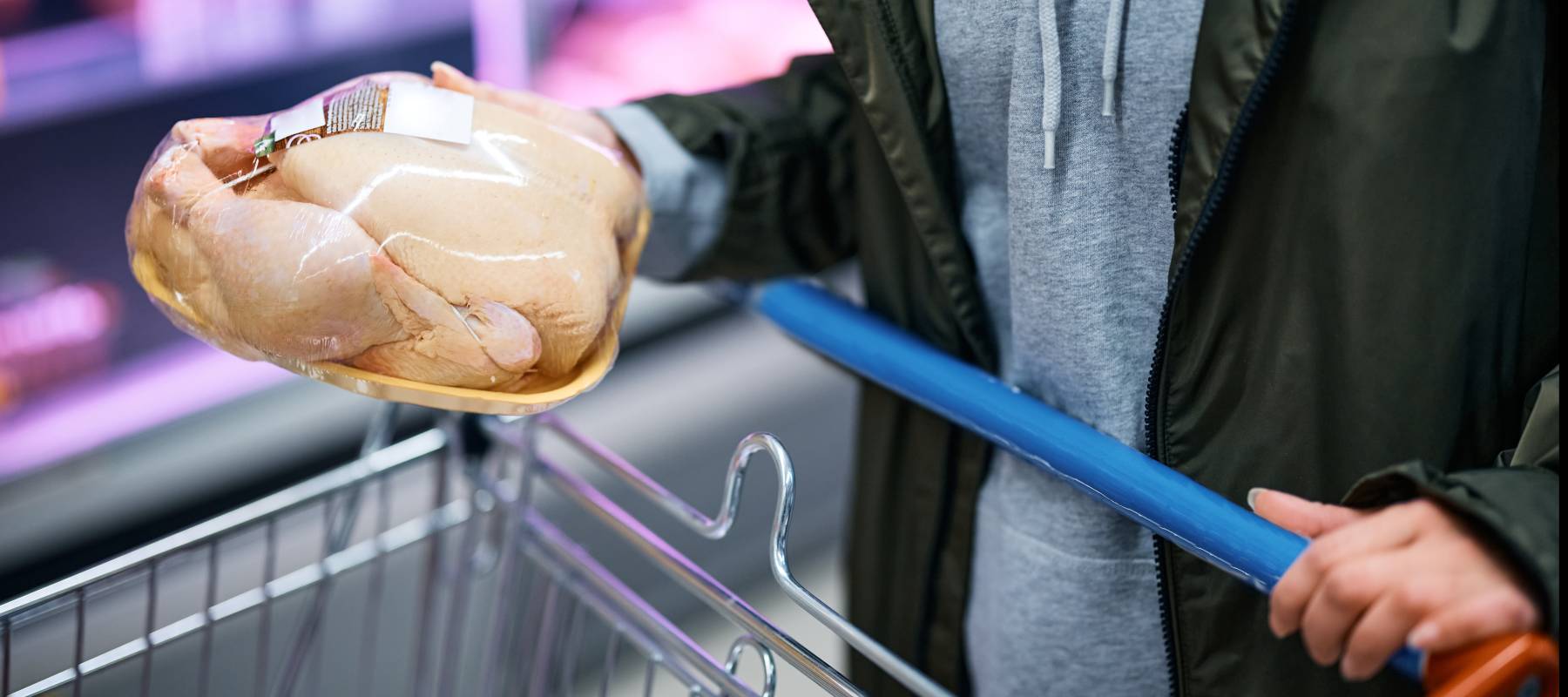 A man holds a small packaged chicken while grocery shopping.