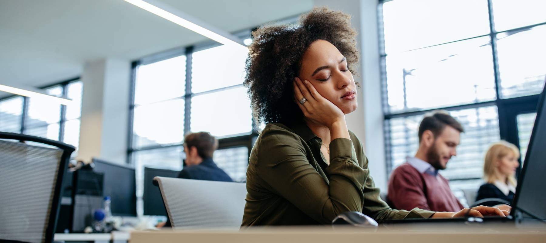 Black woman falling asleep at her desk in a work office environment