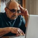 An older man sits on a computer at a restaurant after hours.