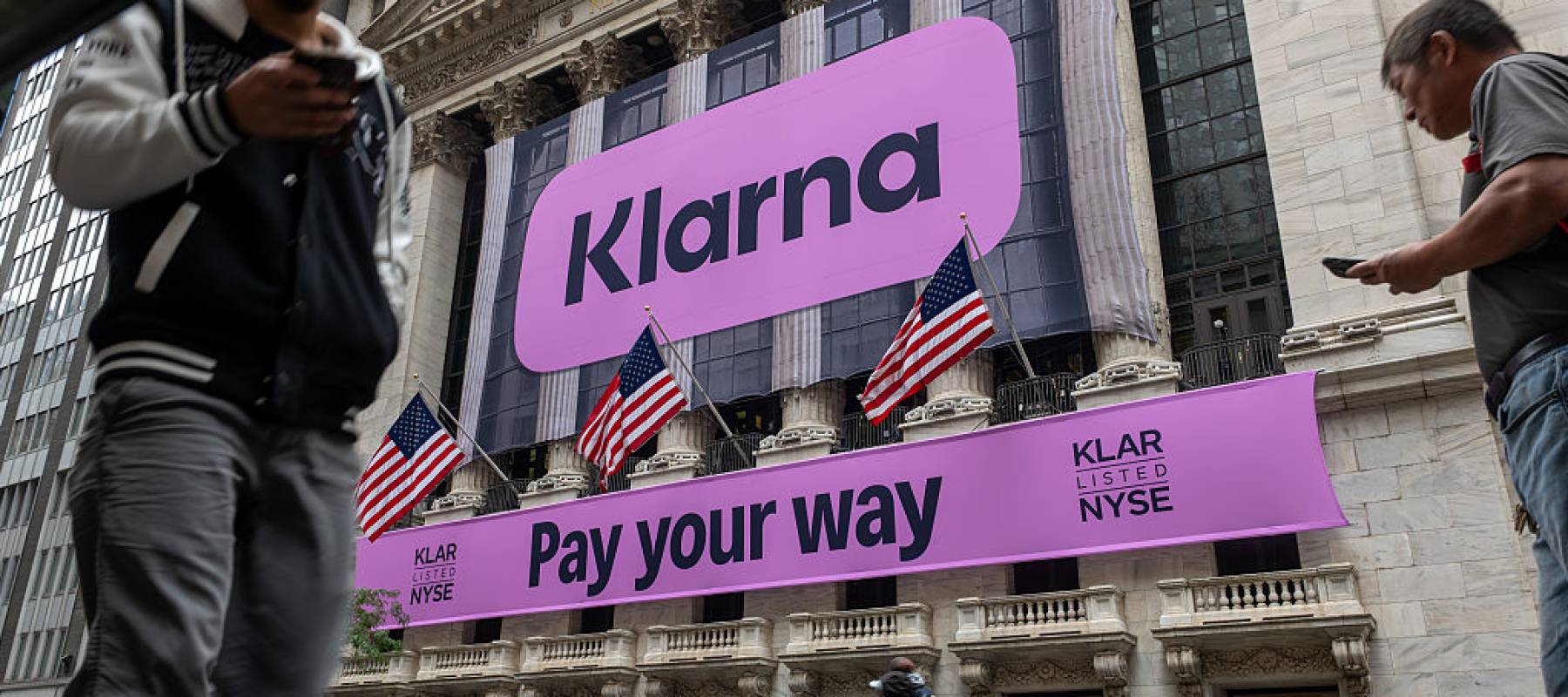 People walk by the New York Stock Exchange featuring a banner for online lender Klarma.