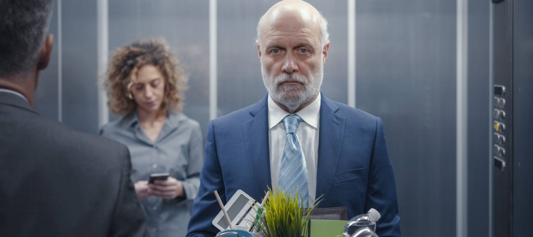 Dejected older man with box of office supplies in an elevator
