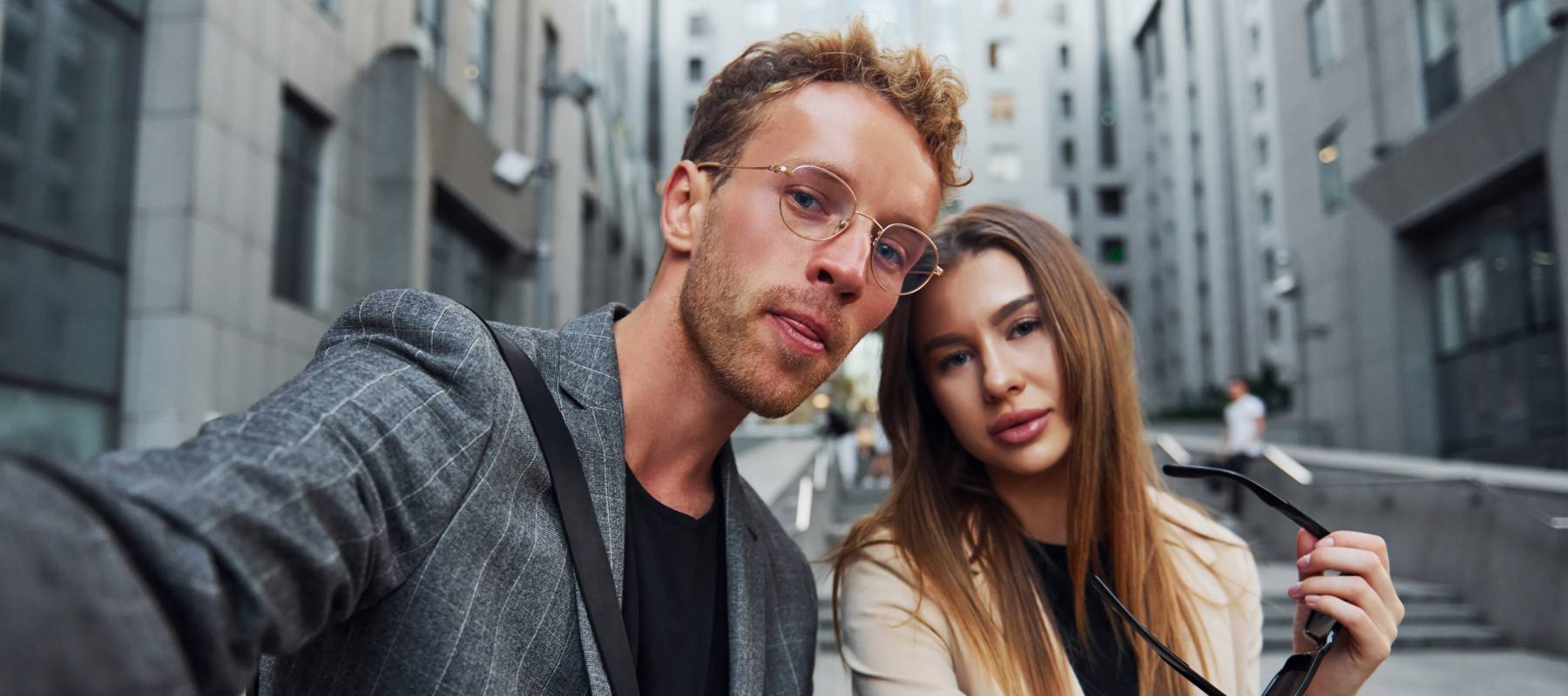 Young, flashy couple taking a selfie in the middle of a building complex.