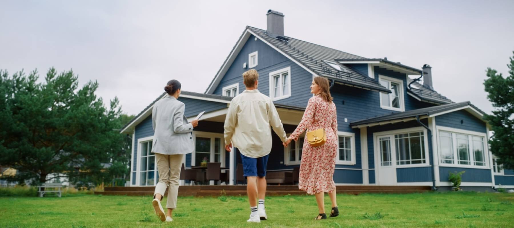 Real Estate Agent Showing a Beautiful Big House to a Young Successful Couple. People Standing Outside on a Warm Day on a Lawn, Talking with Businesswoman, Discussing Buying a New Home.