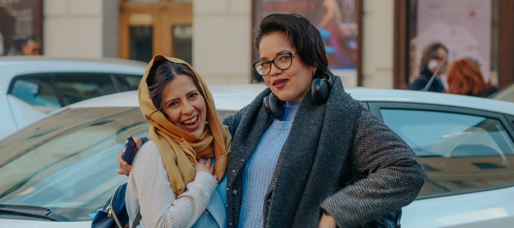 Two women smiling and posing for a photograph on a busy city street with cars in the background.