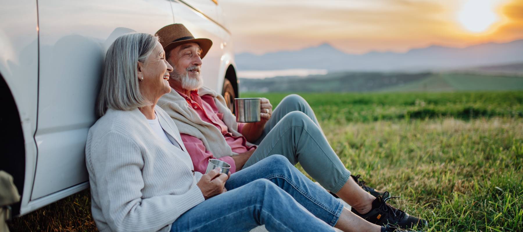 senior Caucasian couple sitting by car and drinking coffee after long drive during their roadtrip