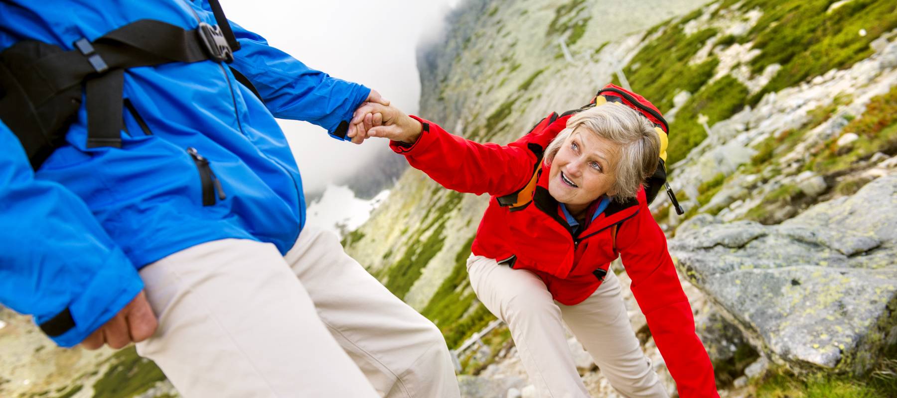 Caucasian senior woman getting a helping hand from her male partner on a difficult hiking trail