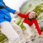 Caucasian senior woman getting a helping hand from her male partner on a difficult hiking trail