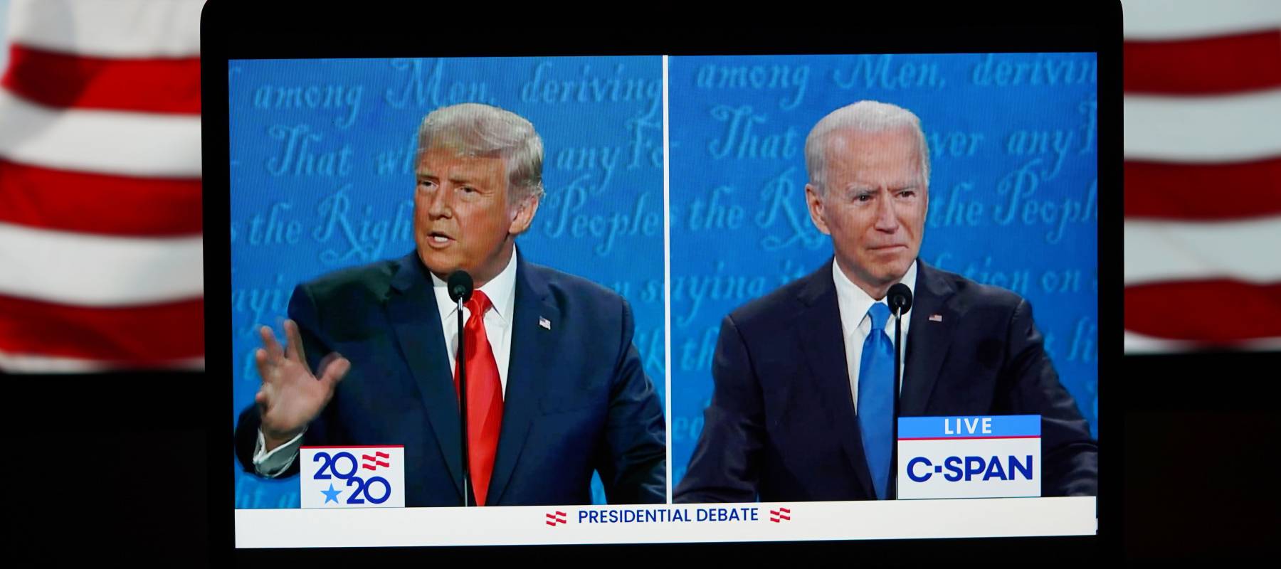 President Trump and Joe Biden at debate, as seen on a split screen tablet with American flag in the background